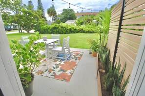 Eine Terrasse im Freien mit Tisch und Stühlen, umgeben von Blumentöpfen und einer Zierdecke.