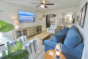 Ein Wohnzimmer mit Fernseher, Sofa, Sesseln und Deckenventilator.
