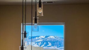 Ein Zimmer mit großem Fenster und Blick auf eine gebirgige Landschaft, einer Deckenleuchte und einer sichtbaren Steckdose.