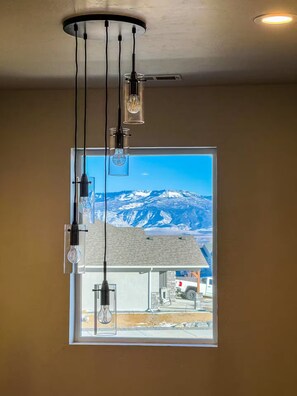 Ein Zimmer mit großem Fenster und Blick auf eine gebirgige Landschaft, einer Deckenleuchte und einer sichtbaren Steckdose.
