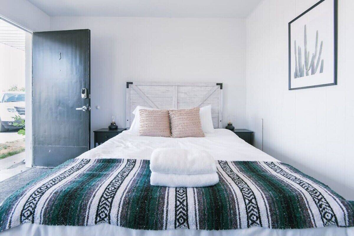 A bedroom with a bed, a headboard, a nightstand, a door, and a framed picture on the wall.