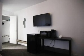 Una stanza con una TV a schermo piatto montata a parete, una scrivania nera con un computer e una decorazione con un cactus.