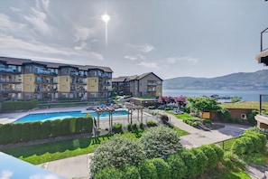 A residential building with a swimming pool, a view of the water, and a mountain in the background. - Lakefront Pool and Lake View 2 Bdrm 4205 (West Kelowna)
