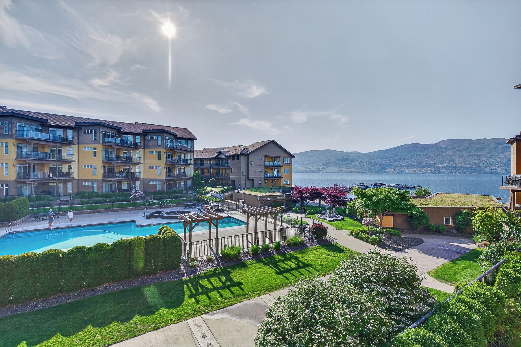 A residential building with a swimming pool, garden, and views of a lake and mountains.