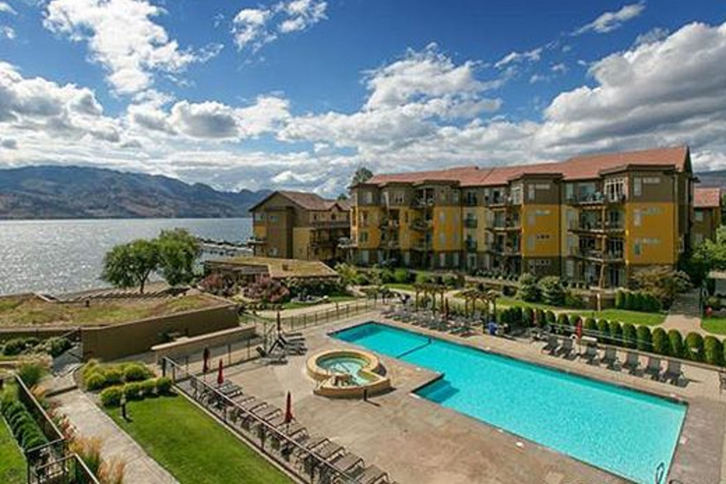 Un hotel con piscina, vistas al lago y montañas al fondo.