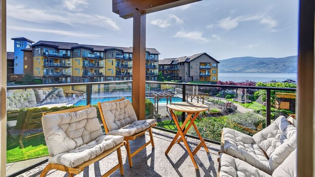 A balcony with outdoor seating, a pool, and a view of multi-story buildings. - Lakefront Pool and Lake View 2 Bdrm 4205 (West Kelowna)