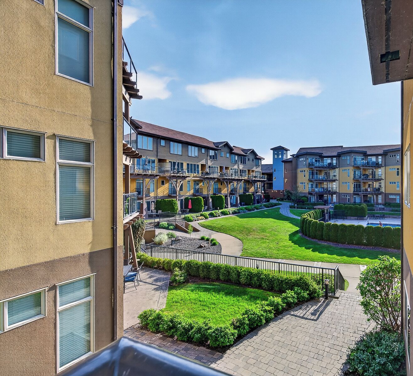 A residential building with multiple balconies, a central courtyard with a lawn, and a paved walkway.
