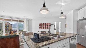 A modern kitchen with a granite countertop, white cabinetry, and a stainless steel refrigerator. - Lakefront Pool and Lake View 2 Bdrm 4205 (West Kelowna)