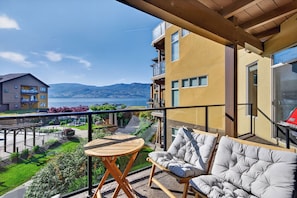 A balcony with a table and two chairs, overlooking a body of water and mountains. - Lakefront Pool and Lake View 2 Bdrm 4205 (West Kelowna)