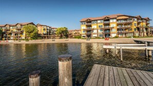 A waterfront hotel with multiple-story buildings, a dock, and a clear sky. - Lakefront Pool and Lake View 2 Bdrm 4205 (West Kelowna)