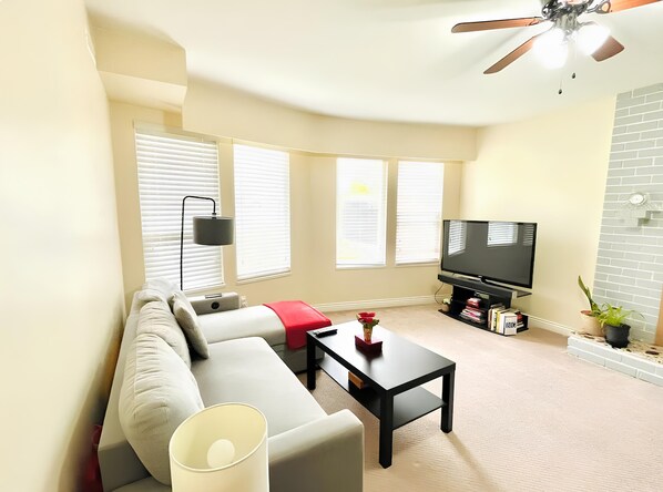 A modern living room with a sofa, coffee table, TV, and a ceiling fan. - Green Gables Resort (Osoyoos)