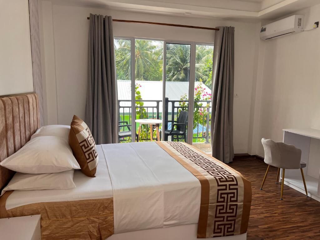 Habitación de hotel con cama, escritorio y balcón con vistas a zonas verdes.