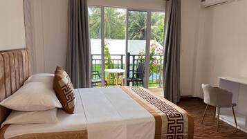 Habitación de hotel con cama, escritorio y balcón con vistas a zonas verdes.