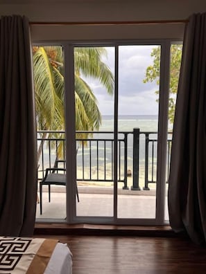 A room with a large sliding glass door leading to a balcony with a view of the ocean and palm trees. - Alma Maldiva beach hotel (Dhidhdhoo)