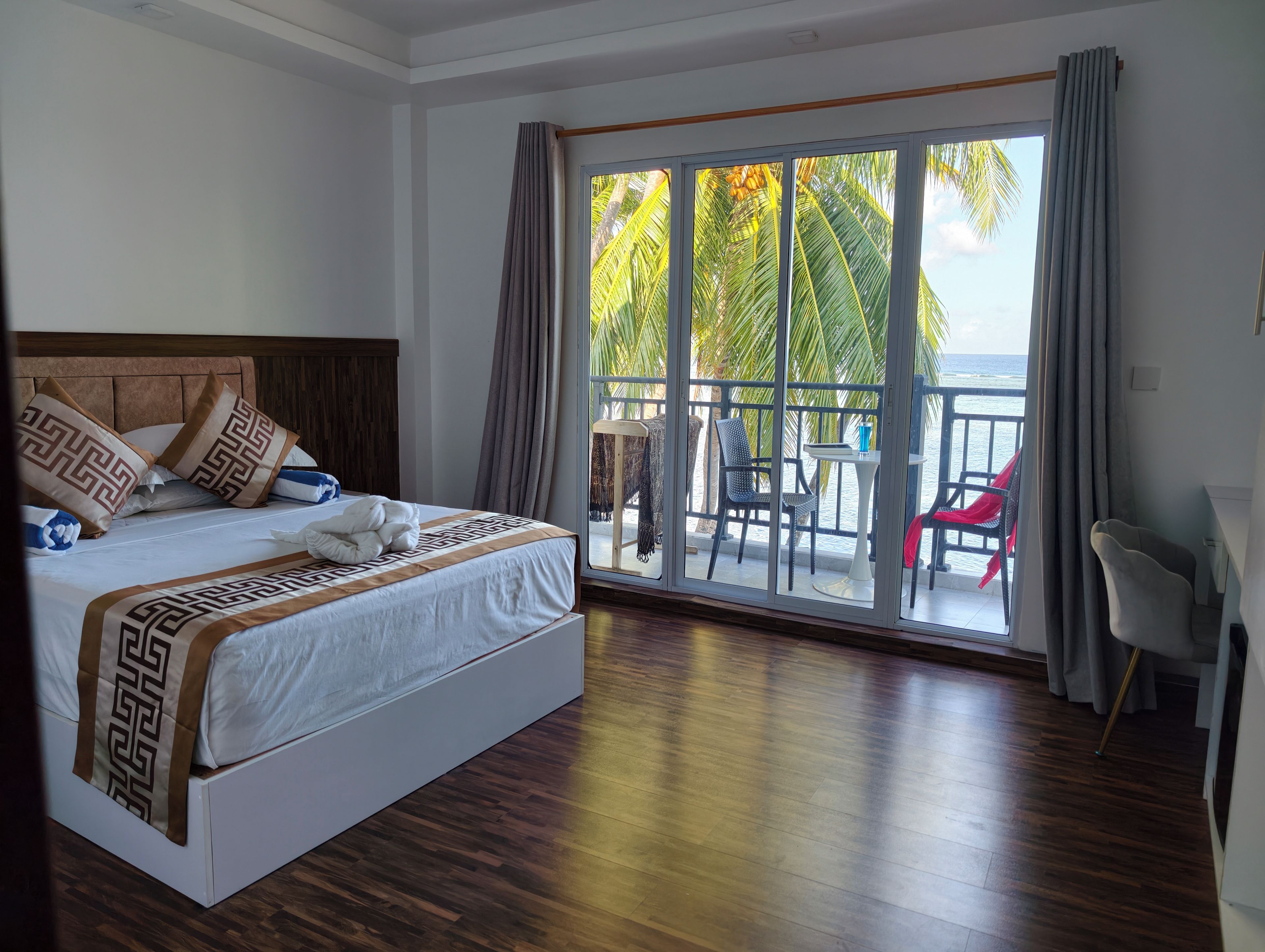 Habitación de hotel con cama, balcón con mesa y sillas, y vista al mar.