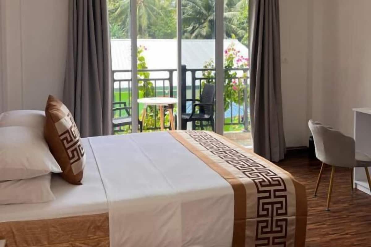 Une chambre d’hôtel avec un lit, un bureau et une vue sur un balcon aménagé avec du mobilier d’extérieur.