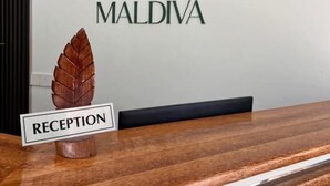 A reception desk with a sign reading 'RECEPTION' and the logo 'ALMA MALDIVA' on the wall behind. - Alma Maldiva beach hotel (Dhidhdhoo)