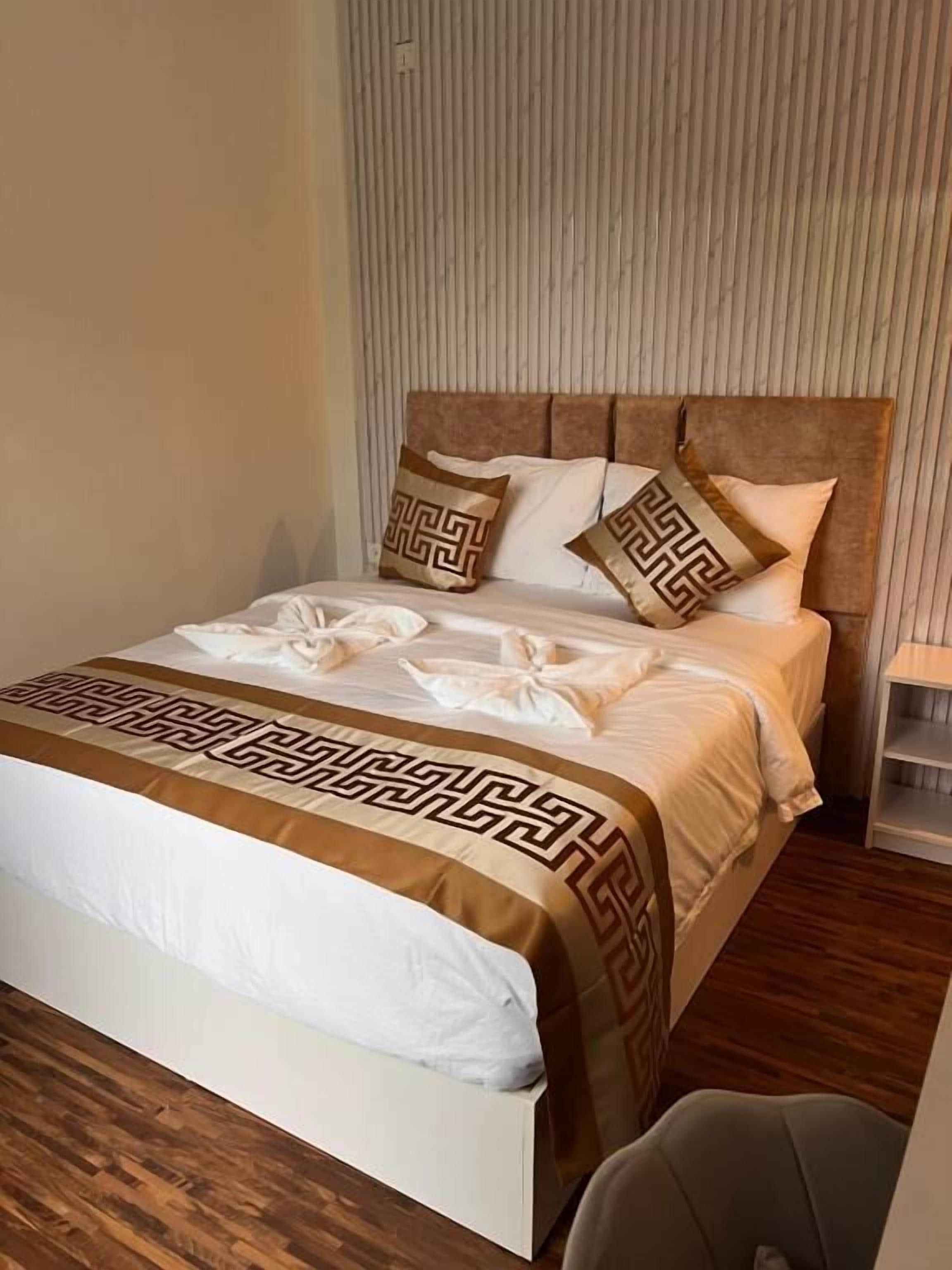 Una cama bien hecha con colcha estampada, cabecera y almohadones decorativos.