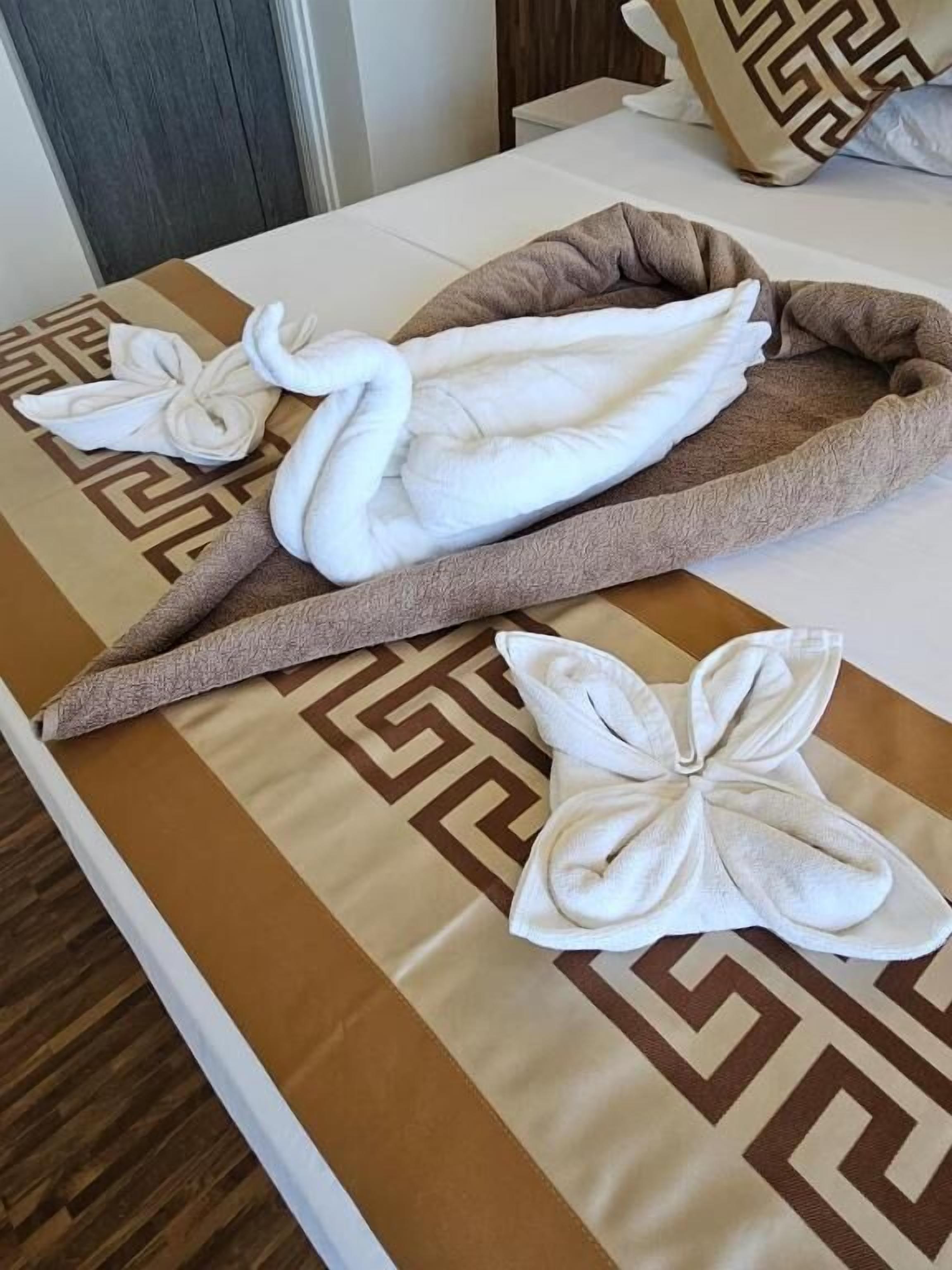 Ein Bett mit einem gemusterten Überwurf, einer braunen Decke und dekorativen Handtüchern in Form von Schwänen und Blumen.