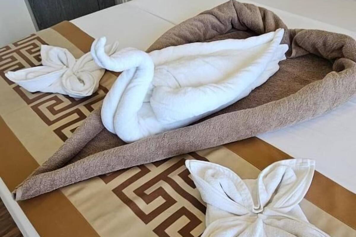 Un lit avec une couvre-lit à motifs, un plaid marron et des serviettes décoratives en forme de cygnes et de fleurs.