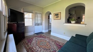 Una sala de estar con televisión, un tapete estampado, un sofá y un cuadro en la pared.