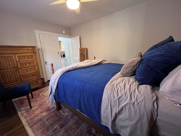 Un dormitorio con cama, cómoda de madera, una silla y un ventilador de techo.