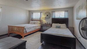 Een slaapkamer met twee eenpersoonsbedden, een nachtkastje met een lamp, een ventilator aan de muur en een decoratief muurkunstwerk.