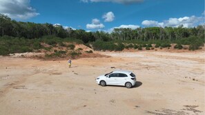 A white car parked on a sandy area with a person standing in the distance.