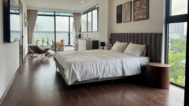 A modern bedroom with a large bed, a seating area, and a view of the city. - 2BR 2BTR Penthouse w/ Kitchen & BBQ Terrace in Long Bien (Hà Nội)