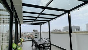 A rooftop terrace with a table and chairs, large windows, and a view of the cityscape. - 2BR 2BTR Penthouse w/ Kitchen & BBQ Terrace in Long Bien (Hà Nội)