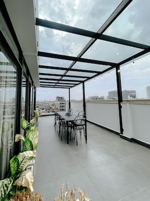 A rooftop terrace with a table and chairs, large windows, and a view of the cityscape. - 2BR 2BTR Penthouse w/ Kitchen & BBQ Terrace in Long Bien (Hà Nội)