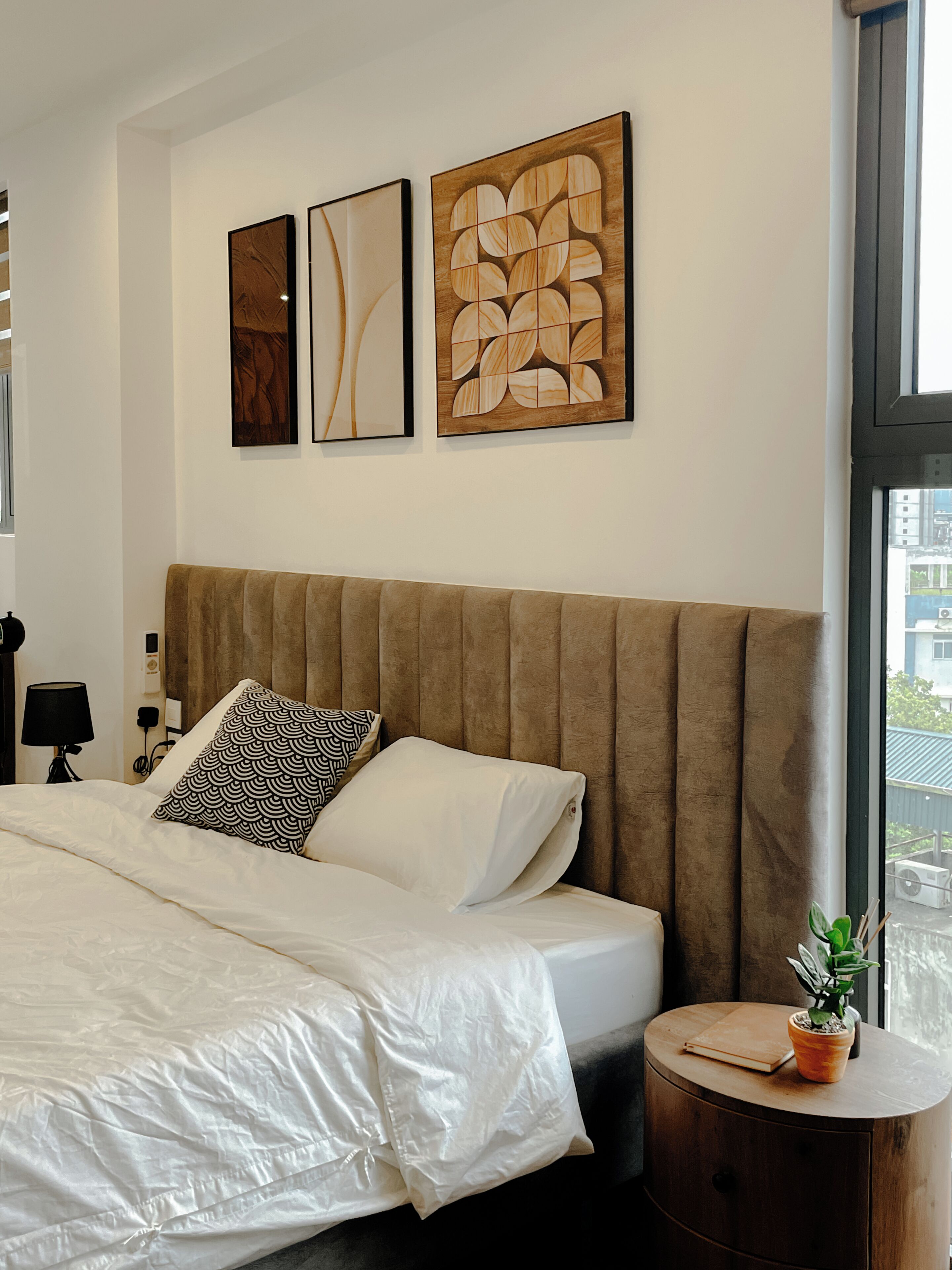 Une chambre à coucher avec un grand lit, une table d’appoint ronde ornée d’une plante et des œuvres d’art accrochées au mur.