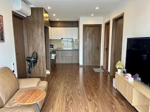 A modern living room with a leather sofa, a small wooden table, a TV, and a kitchen in the background. - Penthouse tầng 7 2BR và Ban công lớn cho tiệc BBQ (Hà Nội)