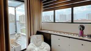 A modern room with a large window, a white chair, a small ottoman, a cabinet, and a decorative vase. - 2BR 2BTR Penthouse w/ Kitchen & BBQ Terrace in Long Bien (Hà Nội)