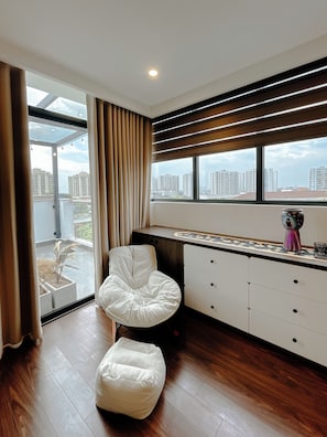 A modern room with a large window, a white chair, a small ottoman, a cabinet, and a decorative vase. - 2BR 2BTR Penthouse w/ Kitchen & BBQ Terrace in Long Bien (Hà Nội)