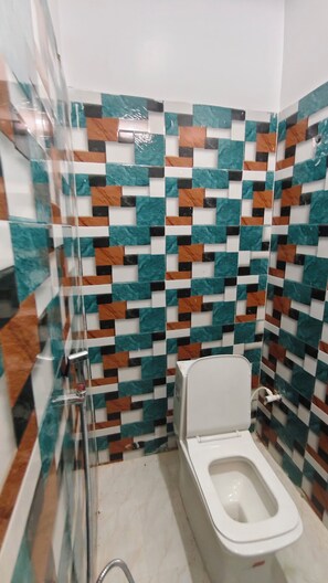 A bathroom with a toilet, a glass shower enclosure, and a tiled wall with a geometric pattern. - Sandhya Guest House (Ekangardih)