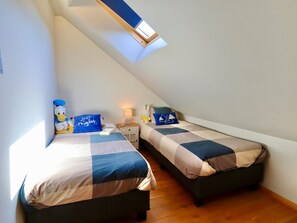 A bedroom with two beds, a skylight, and a small table with a lamp.