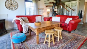 A living room with a red sofa, wooden coffee table, and stools, a large wall clock, and a staircase with a modern design.