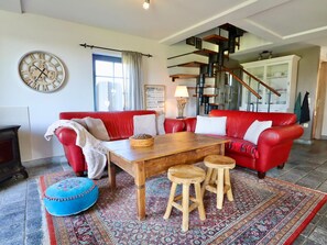 A living room with a red sofa, wooden coffee table, and stools, a large wall clock, and a staircase with a modern design.