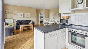 Eine moderne Küche mit weißen Schränken, einer Mikrowelle und einem Backofen. Es gibt eine Essecke mit Tisch und Stühlen sowie ein Wohnzimmer mit Sofa und Couchtisch.