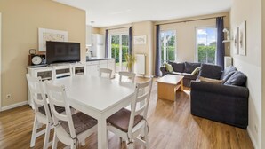 Ein modernes Wohnzimmer mit Esstisch, Stühlen, einer Couch und einem Fernseher.