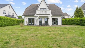 Ein weißes, zweistöckiges Haus mit Balkon, Veranda und gepflegtem Rasen.