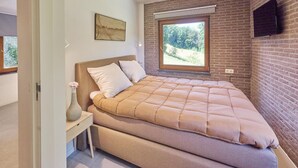A bedroom with a bed, a window, a painting, and a brick wall. - Nice house with a garden and sauna. (Schinnen)