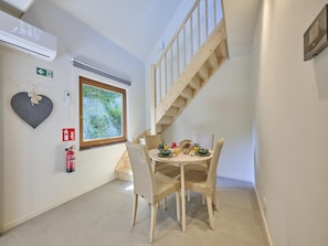 Un comedor con una mesa dispuesta para dos personas, una escalera, un extintor y una ventana con vistas a zonas verdes.