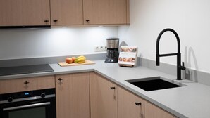 A modern kitchen with wooden cabinets, a black sink, a coffee maker, and a cutting board with fruits. - Nice house with a garden and sauna. (Schinnen)