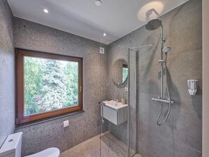Een moderne badkamer met douche, wastafel en toilet, voorzien van een groot raam en een spiegel.