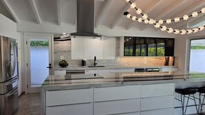Une cuisine moderne dotée d’un grand îlot central, d’appareils électroménagers en acier inoxydable et offrant une vue sur la verdure environnante.
