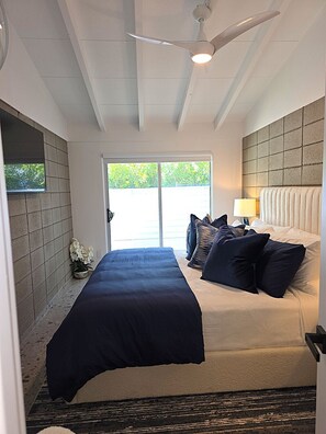 Ein Schlafzimmer mit einem Bett, Kissen, einem Deckenventilator, einem Fenster und einer Wandlampe.