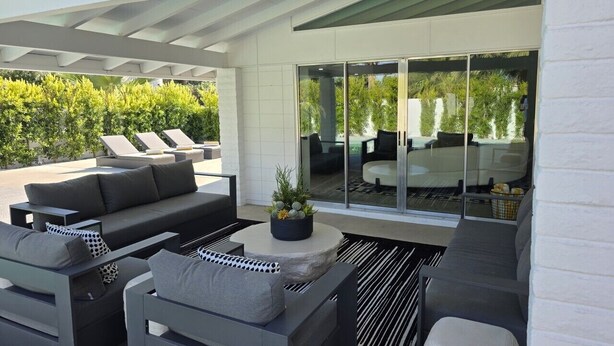 Une terrasse extérieure avec un canapé, une table ronde et une porte vitrée donnant sur un espace piscine.