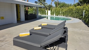 Un espace aménagé au bord de la piscine, avec des chaises longues, un patio couvert et une piscine.